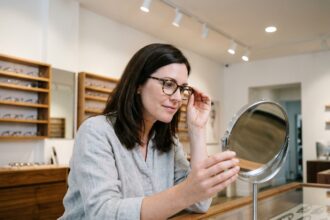 Femme essayant des montures de lunettes chez un opticien moderne, comparant les options disponibles en magasin